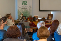 Widzowie siedzący na sali zwróceni w stronę ekranu z prezentacją, którego większość znajduje się po za kadrem. Z lewej strony rollup z widocznym logotypem MKK