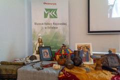 Stolik, na którym leżą pamiątki z podróży do Afryki. Za stolikiem rollup z logotypem MKK oraz Marki Mazowsze. Z prawej niewielki fragment ekranu z wyświetlona prezentacją.