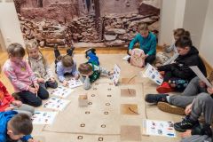 Fragment okręgu, który tworzą siedzące na ziemi dzieci. Rozwiązują karty edukacyjne.