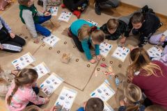 Fragment okręgu, który tworzą siedzące na ziemi dzieci. Rozwiązują karty edukacyjne.