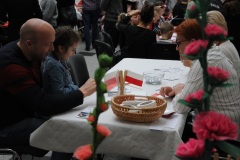 Kilka osób siedzących i rozmawiających przy stole ozdobionym w flagi Polski