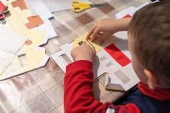 Siedzący przy chłopczyk  skleja z kartonu budynek Muzeum Kultury Kurpiowskiej 
