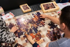 Dwie dorosłe osoby siedzące przy stole i dziecko układają puzzle.