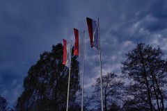 Trzy biało-czerwone flagi na masztach o zmroku.