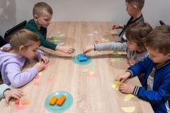 Dzieci siedząc przy stole wykonują tradycyjne ozdoby choinkowe.