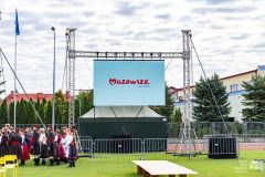 Wielki ekran w plenerze. Przy nim kilkanaścioro osób w strojech ludowych