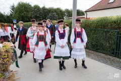 Kilka osób, większość w strojach ludowych. W tle fragment ogrodzenia i budynek