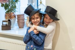 Dwie dziewczynki w czarnych, papierowych kapeluszach pozują do zdjęcia.