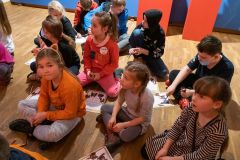 Dzieci siedzą na ziemi i rozwiązują karty edukacujne.