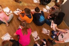 Dzieci siedzą na ziemi i rozwiązują karty edukacyjne. Widok z góry.