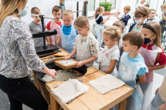 Grupa dzieci stoi przy stanowisku czerpania papieru. Dziewczynka trzyma w dłoniach sito