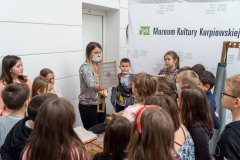 Instruktorka pokazuje grupie dzieci sito do czerpania papieru ze ozdobnym wzorem
