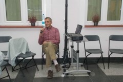 mężczyzna siedzący na krześle w tle okna i krzesła oraz projektor.