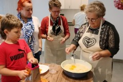 chłopiec ściera marchewkę, 3 kobiety wyrabiają ciasto