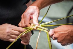 Dłonie dwóch osób wspólnie wyplatających z wikliny