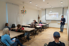 Grupa ludzi słucha wykładu oraz ogląda wyświetlone zdjęcia.
