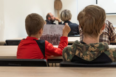 Chłopcy siedzą na wykładzie, jeden ogląda ulotkę.