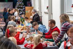 Na muzealnym krytym dziedzińcu przy stołach siedzi lub stoi ponad dwadzieścia osób, dorośli i dzieci, w tym twórcy w strojach kurpiowskich. Uczestnicy spotkania wykonują tradycyjne ozdoby świąteczne. 