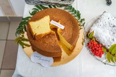 Okrągłe ciasto biszkoptowe przyozdobione zielonymi listkami, ułożone na tacy w kolorze złotym. Obok fragment ciasta prostokątnego posypanego cukrem pudrem