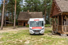 Kamper moda na mazowsze stojąc przodem w skansenie, widać domki.
