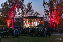 Barwnie oświetlona scena na Fortach Bema, na której odbywa się koncert. Przed sceną tłumnie zgromadzona widownia. Z tyłu widowni repliki armat. Widok po zachodzie słońca.