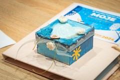 Zdobione pudełeczko leżące na tekturowej teczce z niebieską naklejką