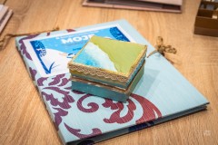 Zdobione pudełeczko leżące na tekturowej teczce z niebieską naklejką i stylową dekoracją