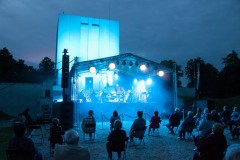 Kilkadziesiąt gości siedzących pod sceną, scena jest koloru błękitna 