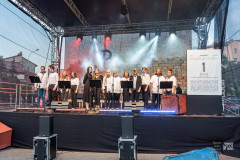 Artyści stoją na scenie, z prawej strony wielka kartka z kalendarza z datą 1 sierpnia, w tle sceny symbol Polski Walczącej.