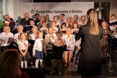 Grupa dzieci i dorosłych śpiewa i daje koncert.