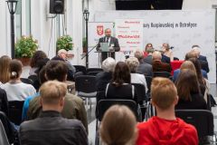Uczestnicy konferencji słuchają przemówienia. W tle mężczyzna stojący przy mównicy