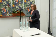 Pani dyrektor Muzeum Kultury Kurpiowskiej przemawia na otwarciu konferencji " Ostrołęckie spotkania historyczne". W tle po lewej stronie kolorowe okna.
