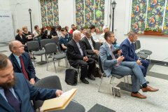 Kilkunasto   osobowa siedząca grupa uczestników  konferencji  słucha odczytu. Za nimi po prawej stronie widnieją kolorowe okna .  