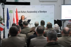 Kobieta stoi przy mikrofonie przed widownią w dziedzińcu muzealnym w tle napis MKK