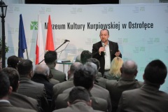 Mężczyzna stoi przy mikrofonie przed widownią w dziedzińcu muzealnym w tle napis MKK