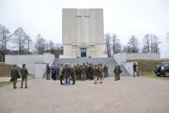 Kobieta stoi przed grupą osób w tle  Pomnik Mauzoleum Żołnierzy poległych w bitwie pod Ostrołęką 