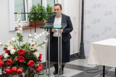 Dyrektor Muzeum stoi przy mównicy. Z lewej strony kadru biało-czerwony bukiet kwiatów.