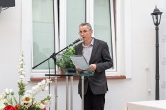 Prelegent stoi przy mównicy. Z lewej strony kadru wyłania się fragment biało-czerwonego bukietu kwiatów.