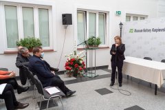 Prelegentka w trakcie wykładu stoi przed publicznością. W tle okna i fragment  ścianki z nazwą Muzeum oraz logotypami. Z lewej strony widać kilka osób z  widowni.