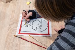 Dłoń malująca pędzelkiem po szkle. Wypełnia kolorem kontury dawnego herbu Ostrołęki