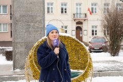 Kobieta mówi do mikrofonu na tle pomnika i budynku