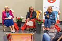 Trzy kobiety siedzące na leżakach, kobieta po prawej stronie trzyma w ręku książkę , Z nimi stoi baner Marszałek Województwa Mazowieckiego.