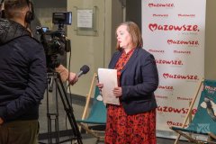 Pani dyrektor Muzeum Kultury Kurpiowskiej w Ostrołęce udziela wywiadu przed kamerami na tle banera z napisem Mazowsze serce Polski.