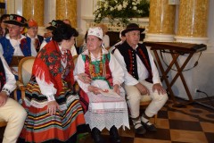 Grupa ludzi siedzi w kurpiowskich strojach.