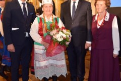 Czwórka ludzi na zdjęciu, kobieta stoi z kwiatami.