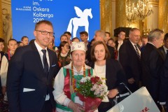 Kobieta trzymając kwiaty pozuje z ludźmi do zdjęcia.