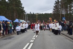 Procesja z palmami wielkanocnymi. Pierwsi idą księża i ministranci w komżach. Mężczyzna z przodu trzyma pionowo krzyż.