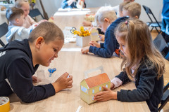 Dzieci siedząc przy stole wykonują z kartonu lampiony w kształcie budynku Muzeum.