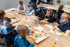 Dzieci siedząc przy stole wykonują z kartonu lampiony w kształcie budynku Muzeum
