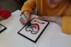 Uczestniczka zajęć tworzy biało-czerwone serce techniką malowania na szkle